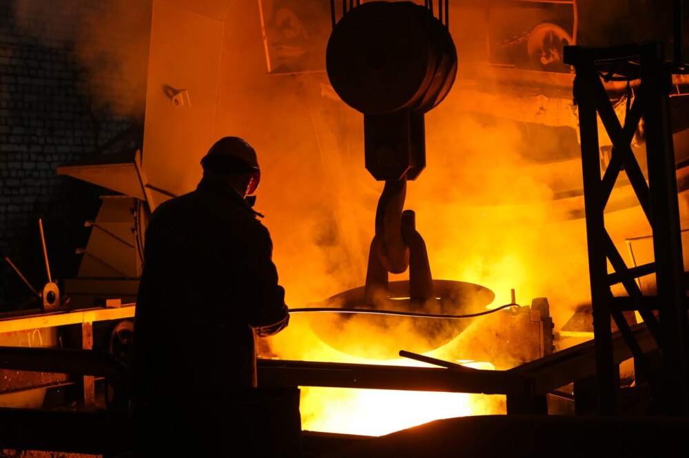 silhouette of man in helmet standing near steel melting pool